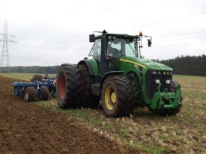Ein großer Traktor zieht auf einem Acker einen schweren Pflug hinter sich her.